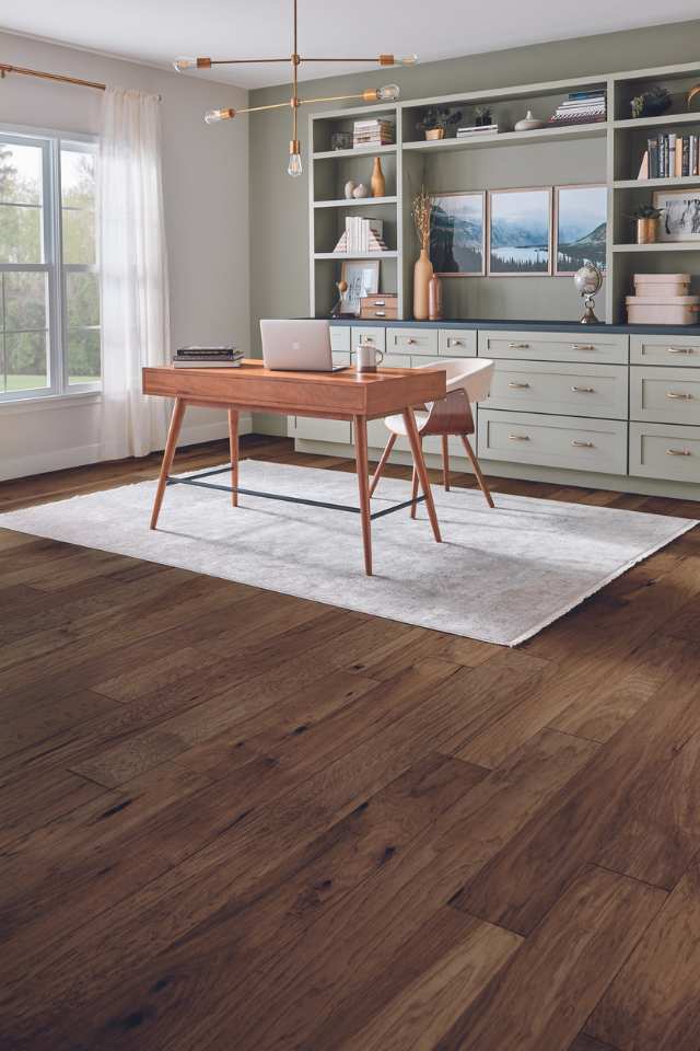 hardwood flooring and area rug in modern home office with sage green accent wall and custom built shelving